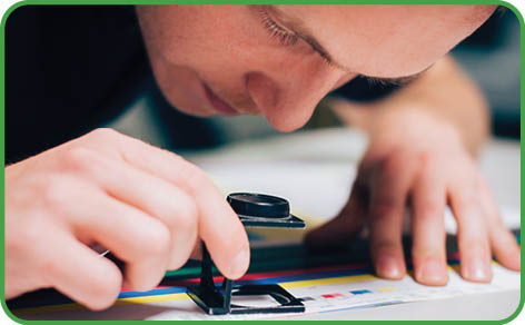Worker in a printing and press centar uses a magnifying glass and check the print quality